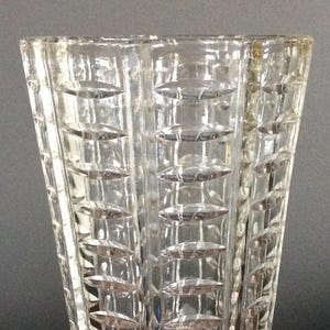 Puede incluir: Un jarrón de vidrio transparente con un patrón geométrico. El jarrón es alto y delgado, con una boca ancha y una base estrecha.