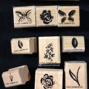 May include: A set of ten wooden stamps with various designs, including flowers, butterflies, leaves, and a palm tree. Each stamp has the text "©2001 STAMPIN' UP!" printed on it.