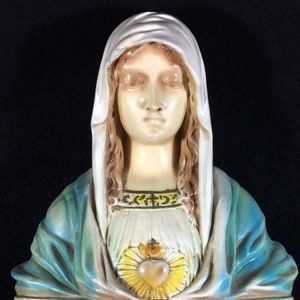 May include: A white plaster bust of the Virgin Mary with a blue and green robe. She has a crown of thorns and a heart with a golden halo.
