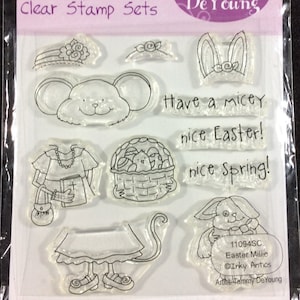 May include: Clear stamp set by Inky Antics featuring Easter-themed designs. Includes a mouse face, bunny ears, a basket of eggs, a bunny, and phrases like "Have a micey" and "nice Easter!" The set is packaged in a clear plastic sleeve.