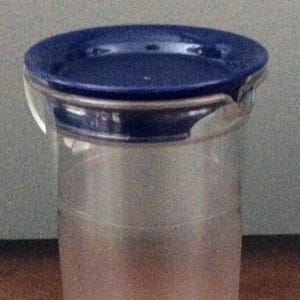 May include: A clear plastic pitcher with a blue lid. The pitcher has a wide mouth and a narrow base.