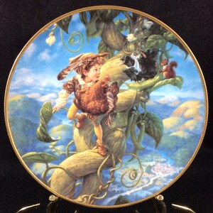 Puede incluir: Un plato de porcelana con una ilustración colorida de un niño escalando una planta de judía. El niño lleva una gallina marrón y una hoja verde. También se representa un pájaro negro y una ardilla en la planta de judía. El plato tiene un borde dorado y un fondo azul.