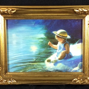 May include: A framed painting of a young child wearing a straw hat sitting on a rock by a lake, holding a stick in the water. The lake is blue and green, and the sky is a light blue.