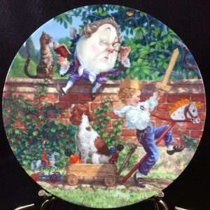 May include: A colorful ceramic plate featuring a whimsical illustration of a boy playing with a toy sword and a rocking horse, a dog sitting in a toy wagon, and a character from Alice in Wonderland jumping over a brick wall. The plate is decorated with green leaves and a blue sky.