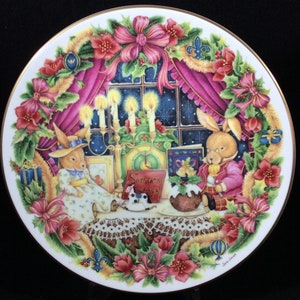 May include: A white porcelain plate with a gold rim features a festive Christmas scene. Two bunnies are sitting at a table with a Christmas pudding, candles, and a book that says "Seasons Greetings". The plate is decorated with holly, berries, and bows.