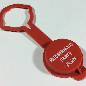 May include: Red plastic bottle stopper with a handle. The stopper has the words "Rubbermaid Party Plan" printed on it.