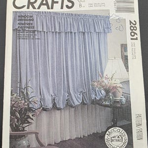 May include: A vintage sewing pattern for window dressing, featuring a blue curtain design with gathered fabric and a ruffled valance. The pattern includes the text "CRAFTS" and "WINDOW DRESSING". The McCall's Home Center logo is visible.
