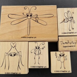 May include: A collection of wooden stamps featuring whimsical insect designs. The stamps include a dragonfly, bee, spider, ladybug, and other stylized bugs. The text "Thankzzzz!" is also present. All stamps are marked with "©2003 STAMPIN' UP!"