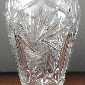 Puede incluir: Un jarrón de vidrio transparente con un diseño de cristal tallado. El jarrón tiene una boca ancha y una base estrecha.