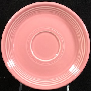 May include: A pink saucer with white rim and three white bands around the edge.