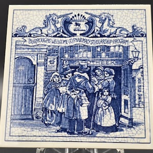 以下が含まれることがあります： 青と白のイラストが描かれた正方形のセラミックタイル。薬局のシーンが描かれており、薬局の店先、当時の服装をした人物、「APOTHEEK」の文字、「BURROUGHS WELLCOME CO. PHARMACY SCHOLARSHIP PROGRAM」の文字が描かれています。