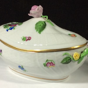 May include: A white porcelain oval serving dish with a lid. The dish is decorated with hand-painted flowers in shades of pink, yellow, blue, and green. The lid features a three-dimensional pink rose with green leaves.