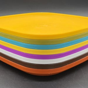 Puede incluir: Una pila de platos cuadrados de colores. Los platos son de varios colores, incluyendo amarillo, verde, turquesa, morado, blanco, marrón y naranja. Los platos están apilados ordenadamente uno encima del otro, creando una exhibición vibrante y llamativa.