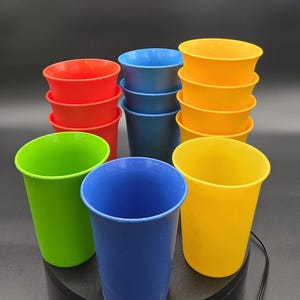 以下が含まれることがあります： 赤、青、黄、緑のカラフルなプラスチックカップのコレクション。 カップは黒い表面に積み重ねられ、配置されており、鮮やかな色とシンプルなデザインが際立っています。 ピクニックや日常使いに最適です。