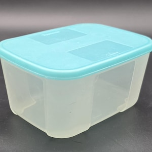 Puede incluir: Un recipiente rectangular de plástico transparente para guardar alimentos con una tapa turquesa. El recipiente tiene un cuerpo ligeramente translúcido y una tapa a juego que encaja perfectamente. La tapa tiene forma rectangular.