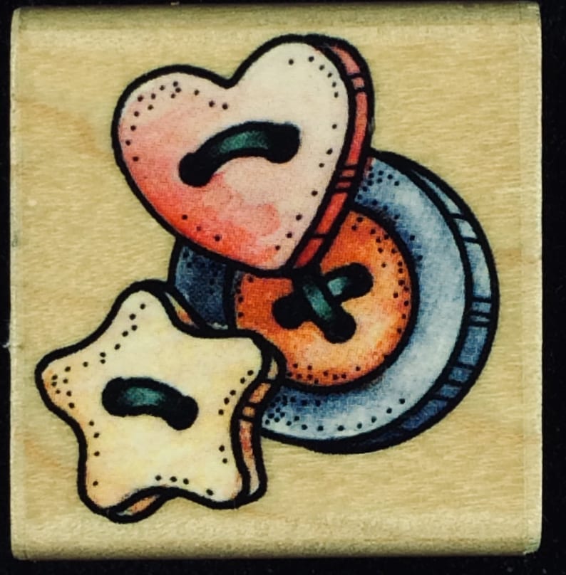 May include: Three fabric buttons in the shape of a heart, a star, and a circle. The heart button is pink and red, the star button is yellow, and the circle button is orange with a blue rim.