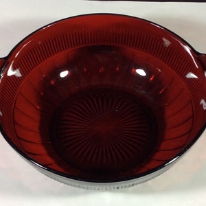 May include: A red glass bowl with two handles. The bowl has a ribbed design and a starburst pattern on the bottom.