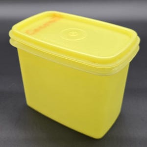 May include: A bright yellow rectangular food storage container with a matching lid. The lid has a small circular indentation in the center. The container is made of plastic and is likely vintage.
