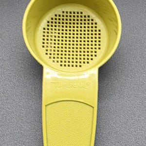 May include: A vintage yellow Tupperware strainer with a perforated bowl and a long handle. The handle has a textured grip and a hole at the end. The Tupperware logo is visible on the handle.
