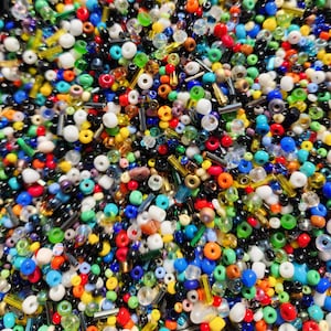 May include: A large assortment of colorful glass beads in various shapes and sizes. The beads are a mix of opaque and transparent colors, including red, blue, green, yellow, and white.