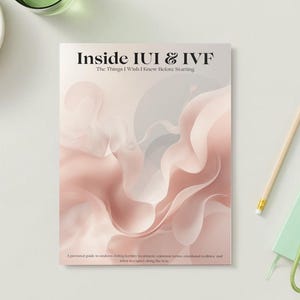 May include: A book titled "Inside IUI & IVF" with abstract pink and white artwork. A pencil, a small green notebook, and a bunch of grapes are also on the white surface. The book's subtitle reads "The Things I Wish I Knew Before Starting."