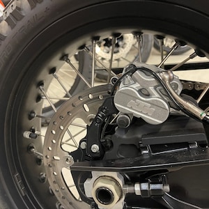 May include: Close-up of a black motorcycle wheel with a silver brake caliper that says "KTM" on it. The wheel has a black tire with the words "Enduro Trail" on it.