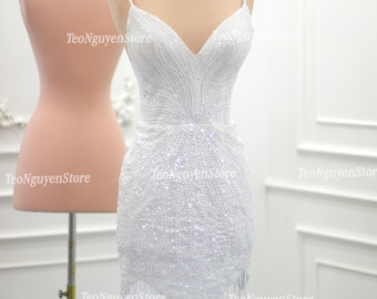 Könnte beinhalten: Ein weißes, perlenbesetztes Minikleid mit V-Ausschnitt und Spaghettiträgern. Das Kleid hat einen Fransen-Saum und befindet sich auf einer Schaufensterpuppe.