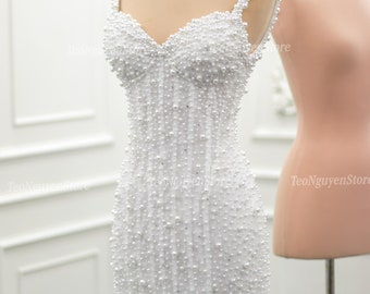May include: A white mini dress with a sweetheart neckline and spaghetti straps. The dress is covered in white pearls.