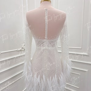 May include: A white mini dress with a beaded bodice and feather trim. The dress has long sleeves and a fitted silhouette.