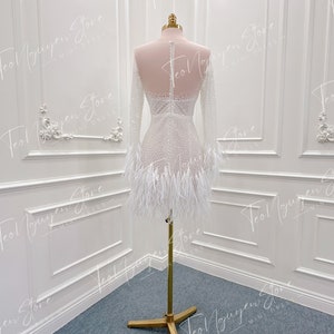 May include: A white mini dress with long sleeves and a feather trim. The dress is beaded and has a fitted silhouette.