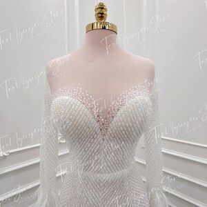 May include: A white beaded long-sleeved wedding dress with a sweetheart neckline and feather trim on the sleeves.