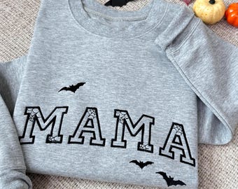May include: Gray sweatshirt with the word "MAMA" in black outlined letters with spiderwebs inside each letter. There are four black bats with spiderwebs on their wings around the word.