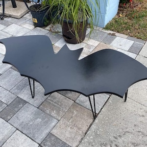 May include: Black bat-shaped coffee table with a black painted finish and thin black metal legs.