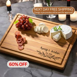 May include: A rectangular wooden serving board featuring a juice groove, engraved with the text Avery & Jordan Est. 2025 and a leafy branch design. The board is topped with a cluster of red grapes, sliced pepperoni, and a wheel of brie cheese.