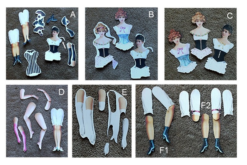 May include: A set of paper doll cutouts featuring a woman in various outfits. The set includes a black and white striped dress, a white dress with a black corset, a white dress with a blue corset, a white dress with a pink corset, and a white dress with a black corset. The set also includes a pair of black stockings, a pair of white stockings, a pair of black shoes, a pair of white shoes, and a pair of arms.