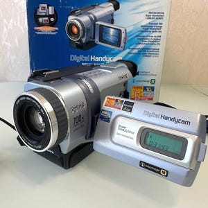 Può includere: Una videocamera Sony Digital8 Handycam color argento con zoom digitale 700x e obiettivo zoom ottico 25x. Il dispositivo è dotato di uno schermo LCD ribaltabile, tecnologia Super SteadyShot e un piccolo display digitale che mostra l'orario 0:31:43.