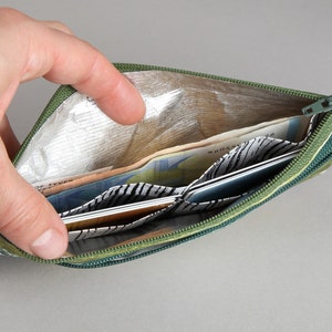 May include: A green zippered pouch with a silver lining is open and filled with cash and cards. The pouch has a black and white patterned lining.