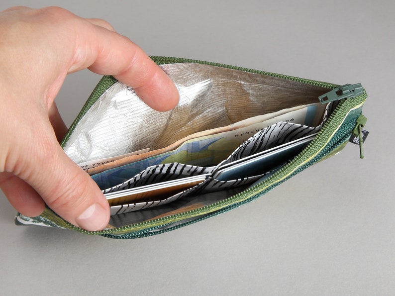 May include: A green zippered pouch with a silver lining is open and filled with cash and cards. The pouch has a black and white patterned lining.
