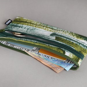 May include: A green and white zippered pouch with a green and white abstract pattern. The pouch is open and filled with cash and cards.