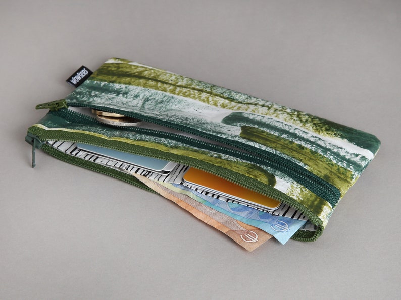 May include: A green and white zippered pouch with a green and white abstract pattern. The pouch is open and filled with cash and cards.