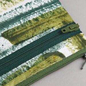 May include: A green and white striped zippered pouch with a green zipper pull. The pouch has a green and white abstract pattern.