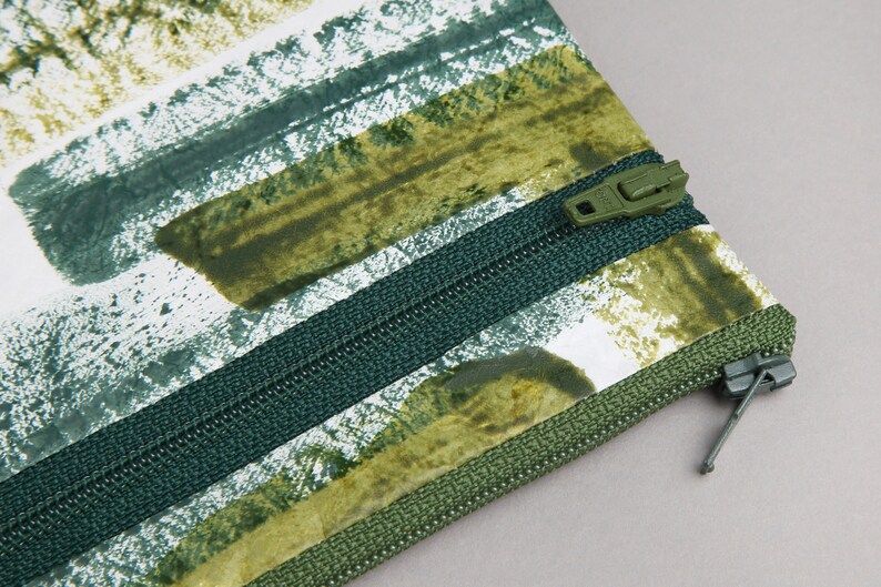 May include: A green and white striped zippered pouch with a green zipper pull. The pouch has a green and white abstract pattern.
