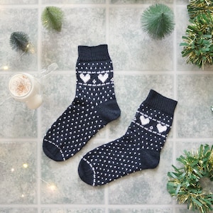 以下が含まれることがあります： 白いハート模様の黒い靴下2足。靴下は編み物で、お祝いの雰囲気があります。