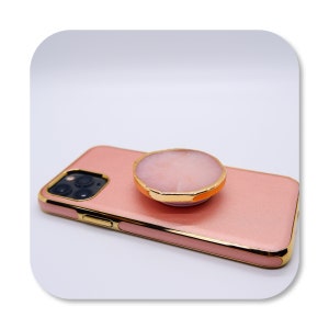 May include: A pink phone case with a gold trim and a pink and gold phone grip.