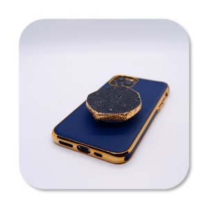 Puede incluir: Una funda de teléfono azul con un borde dorado y un agarre de teléfono negro y dorado.