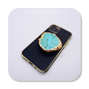 May include: A turquoise and gold phone ring holder attached to a black phone case.