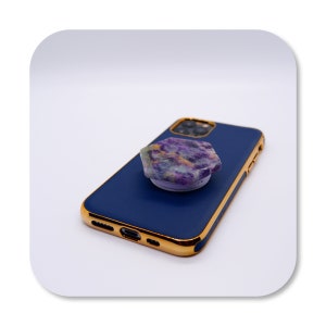 May include: A blue phone case with a gold trim and a purple and green stone phone grip.
