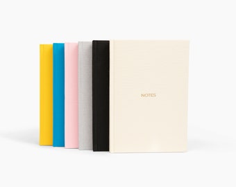 May include: Five notebooks with different colored covers: yellow, blue, pink, gray, and black. The black notebook has the word "NOTES" printed on the front.