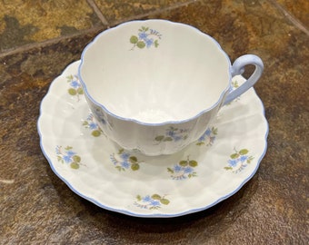 Könnte beinhalten: Ein weißes Tee-Set mit einem blauen Blumenmuster. Tasse und Untertasse haben einen gewellten Rand und einen blauen Saum.
