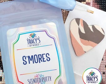 May include: A light blue pouch of S'mores scented putty with a label reading Tracy's DP World S'mores Scented Putty. A light blue diamond painting pen and a heart-shaped piece of putty with brown, tan, and pink swirls are positioned nearby.
